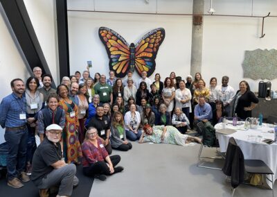An image of a group of 60 people gathered in a large room with a butterfly art piece.